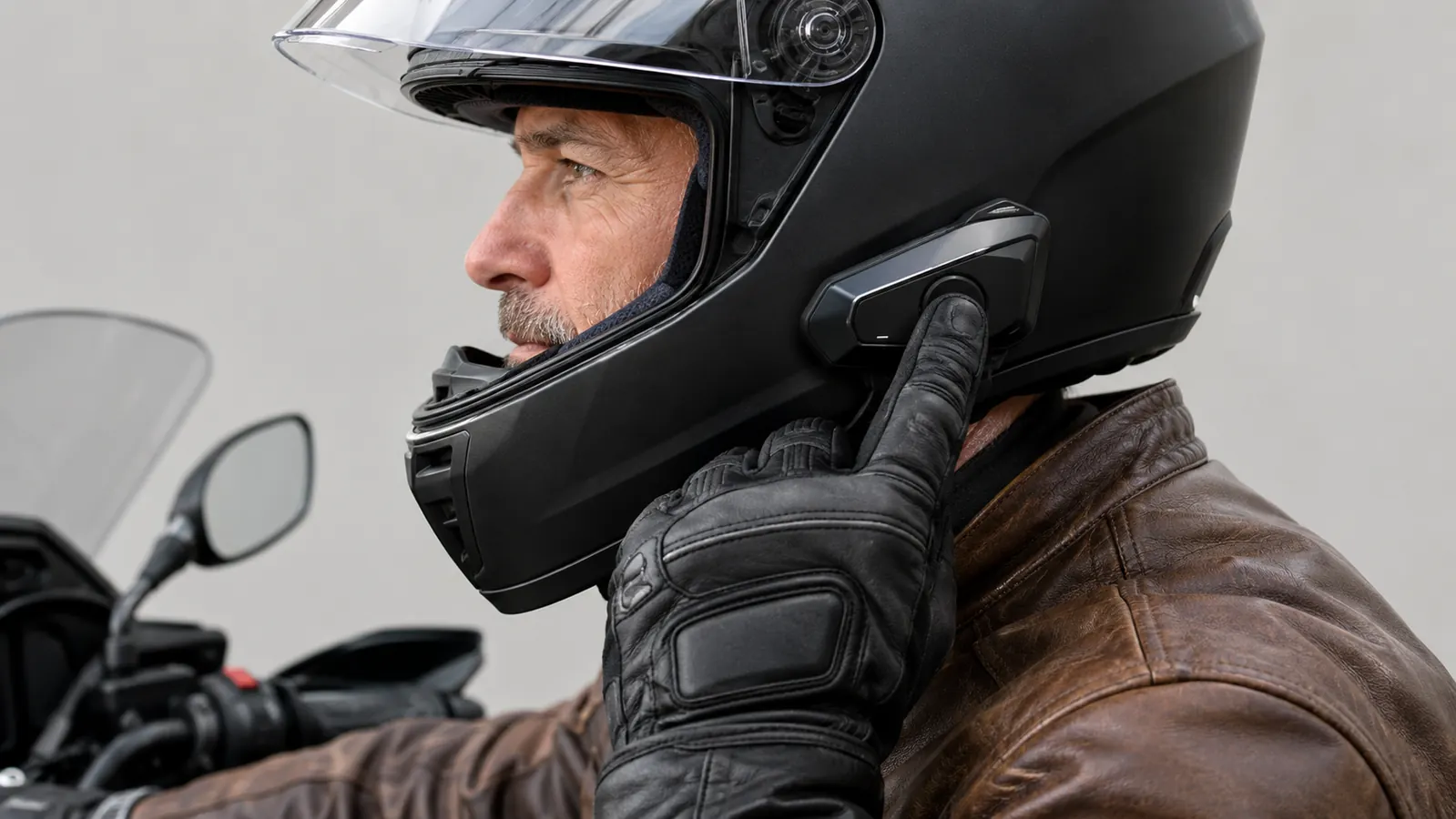 A rider's gloved hand pressing a button on a headset unit mounted to the side of a helmet