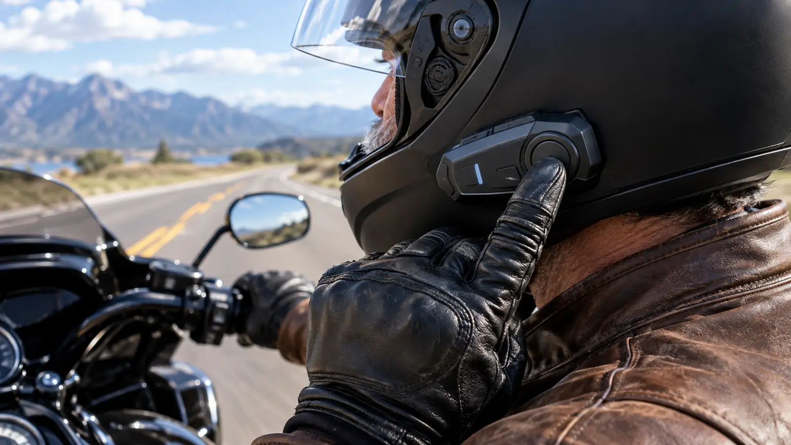 A rider's gloved hand reaching for the control button on a helmet-mounted communication unit