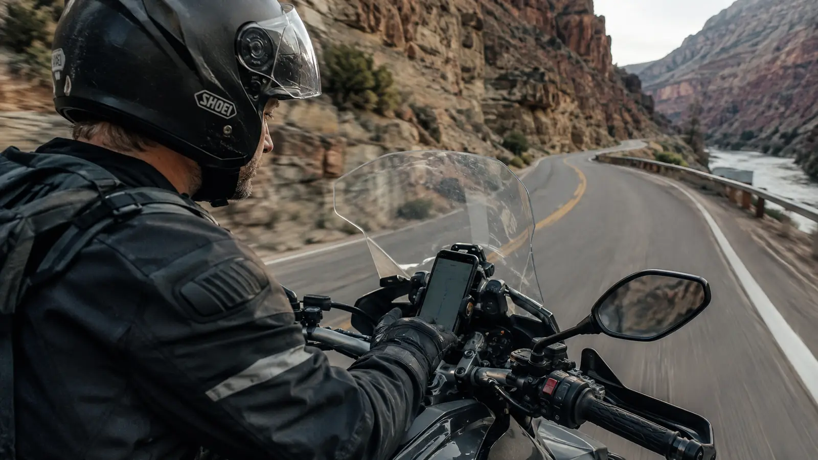A rider glancing at a phone mounted on the handlebar as the road curves through a canyon